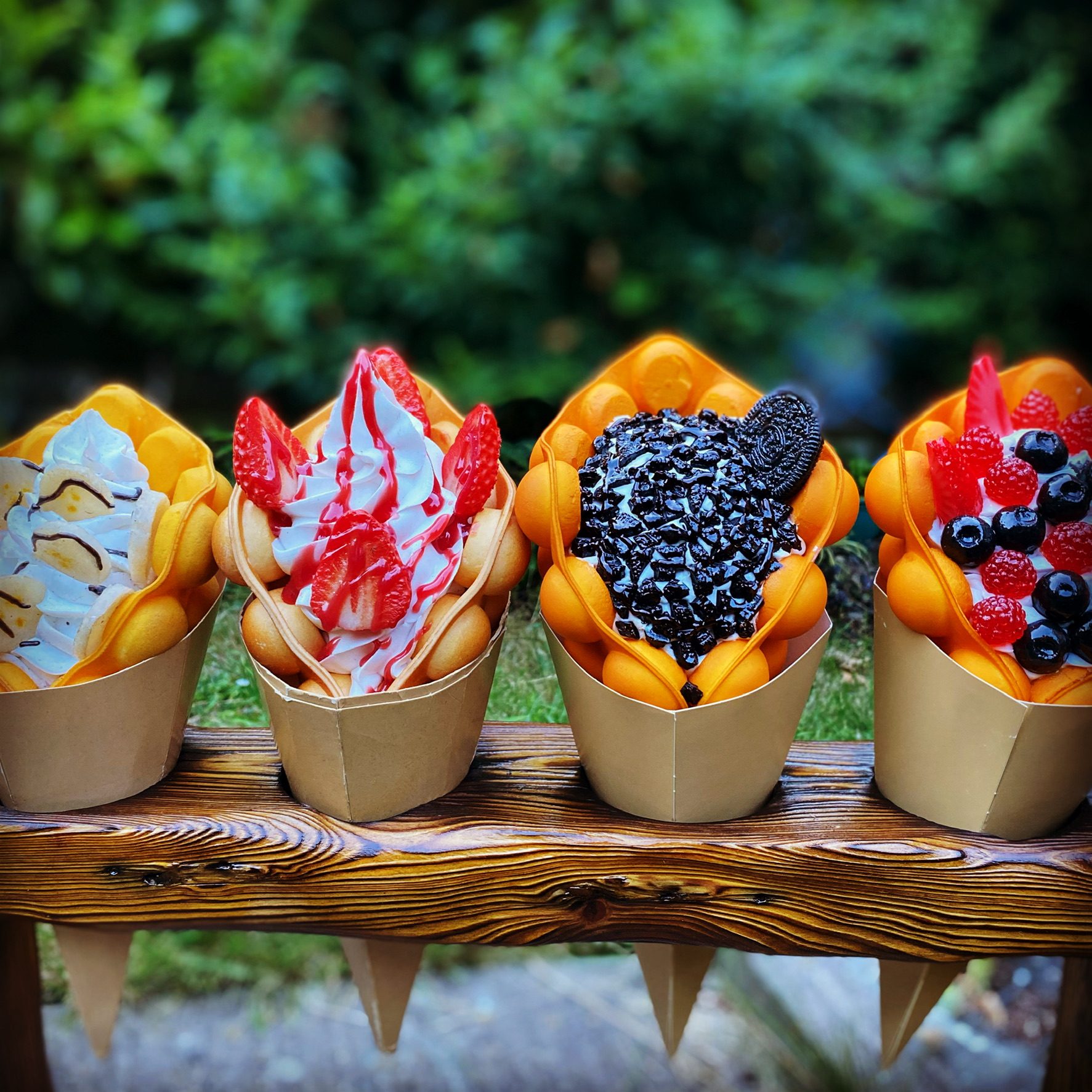 A row of bubble waffles in paper cones, topped with fruit and ice cream