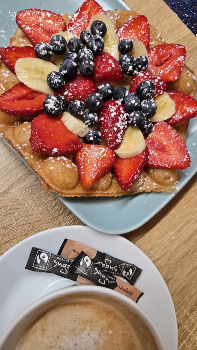 A waffle with strawberries, blueberries and banana, and a coffee